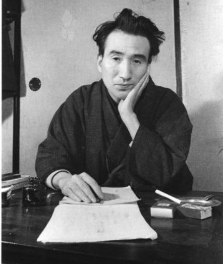 Outra imagem do mesmo homem, mostrando o seu dorso. Ele está vestido em um kimono, na mesma posição. Tem seu punho sobre uma mesa, no qual pende uma pena, e abaixo do qual está um papel. Ele olha diretamente para a câmera.